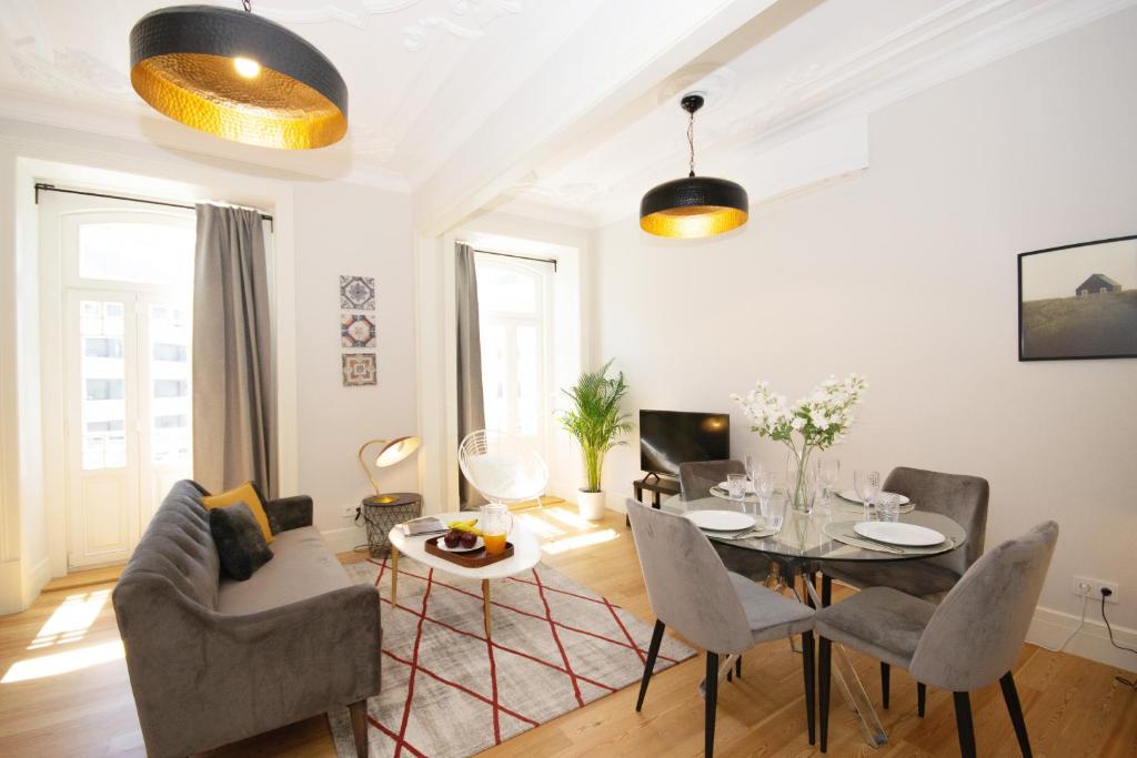 Bright living room with gray sofa, glass dining table, modern chairs, and ceiling lights.
