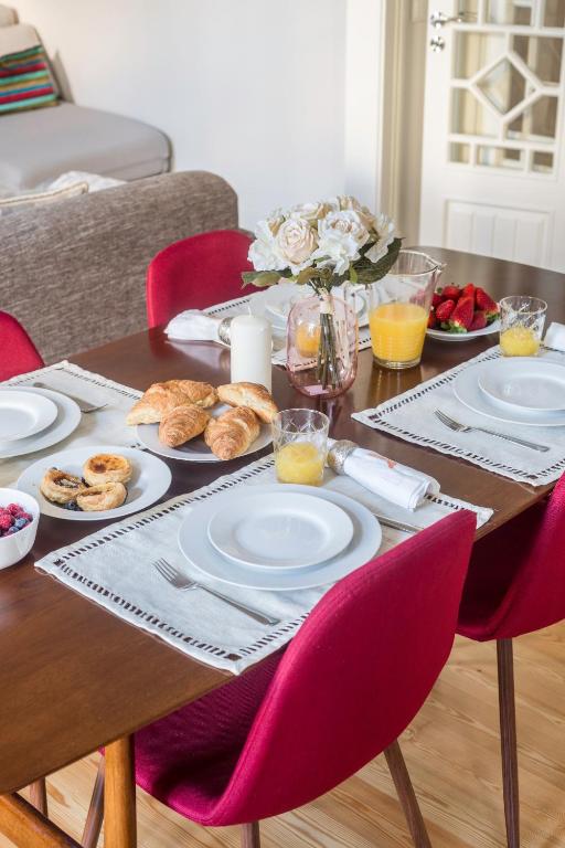 Dining table set with white plates, croissants, juice, strawberries, and a vase of white flowers.