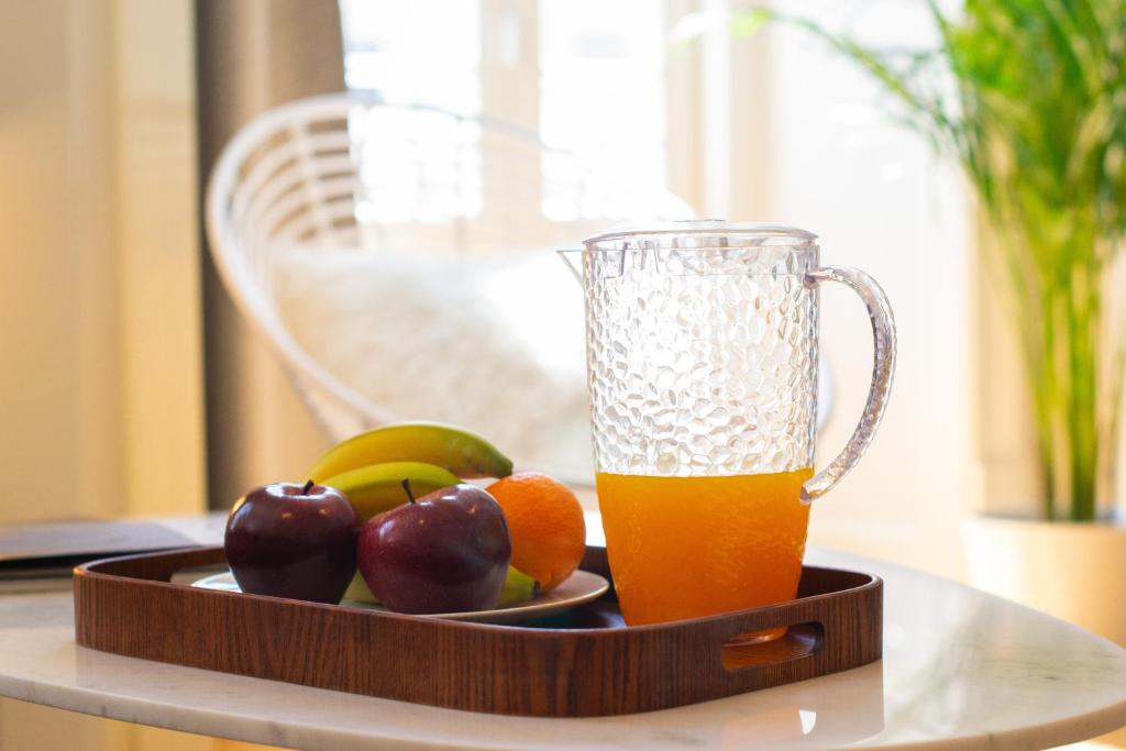 Glass pitcher with orange juice and plate of fruit on a wooden tray on a marble table.