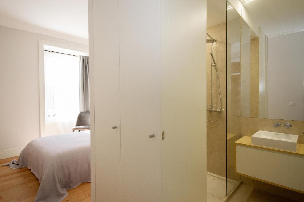 View of a bedroom with a gray bedspread, adjacent white closet, shower, and bathroom sink with mirror.