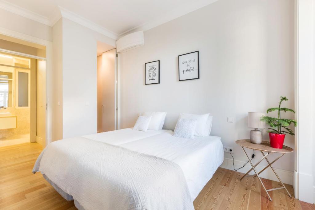 Minimalist bedroom with two beds pushed together, white bedding, wooden floor, a side table with a lamp and plant.