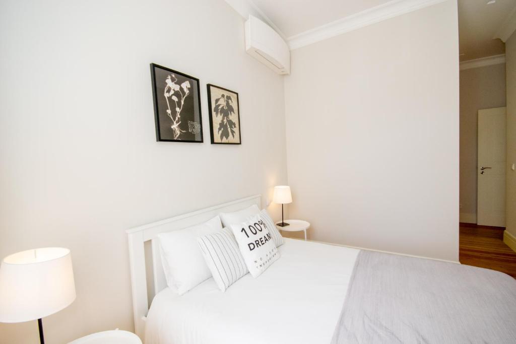 Minimalist bedroom with white bed, pillows, two framed plant prints, a floor lamp, and a table lamp.
