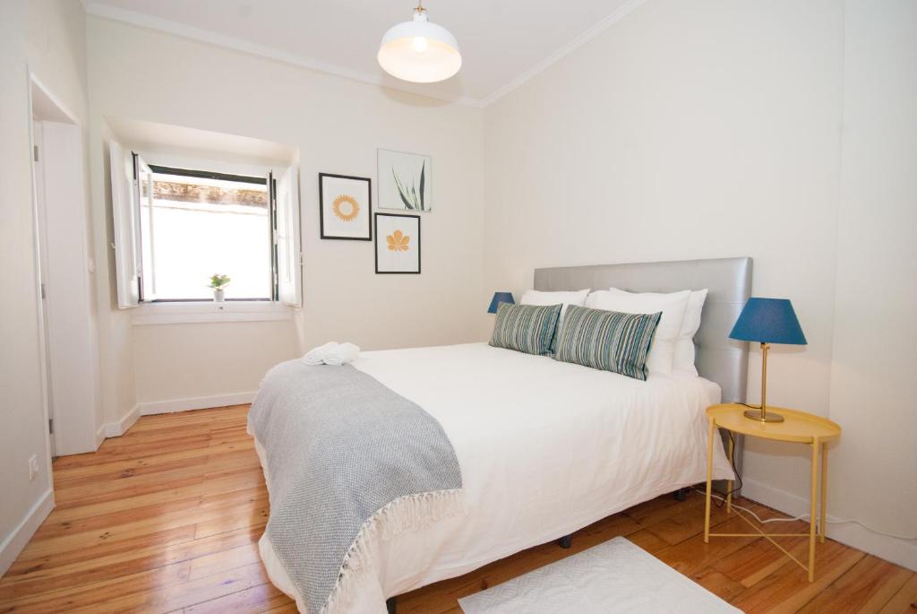 Bright bedroom with a double bed, striped pillows, gray blanket, yellow bedside table, and open window.