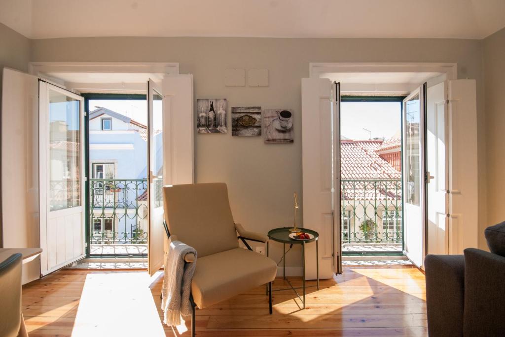 Bright room with open double windows, armchair with a blanket, small table, and wooden floor.
