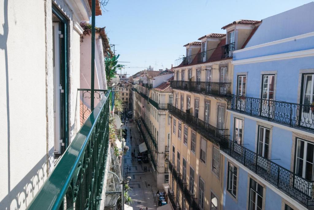 View along balconies of colorful city buildings over a narrow street with people walking.