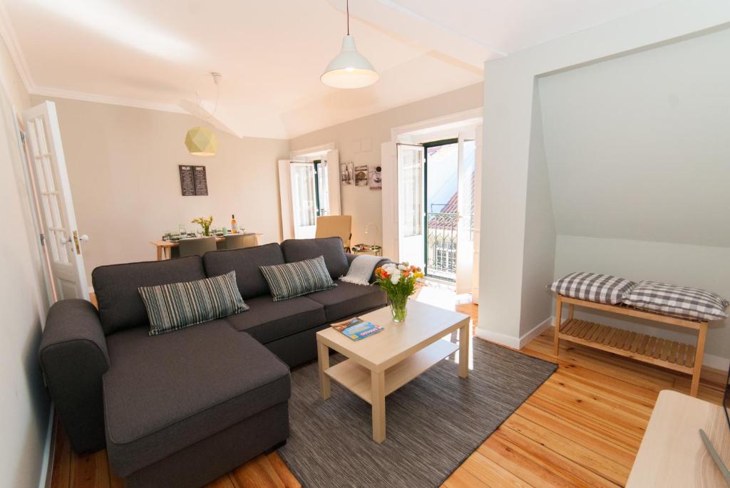 Bright living room with gray sectional sofa, striped pillows, wooden coffee table, and open balcony doors.