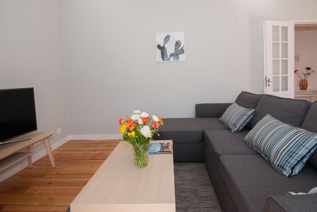 Living room with sectional gray sofa, striped pillows, wooden coffee table with flowers, and TV on stand.