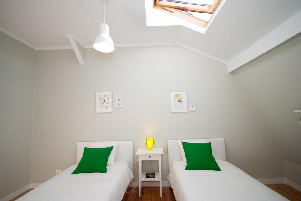 Minimalist room with two single beds, white bedding, green pillows, a nightstand with a yellow lamp.