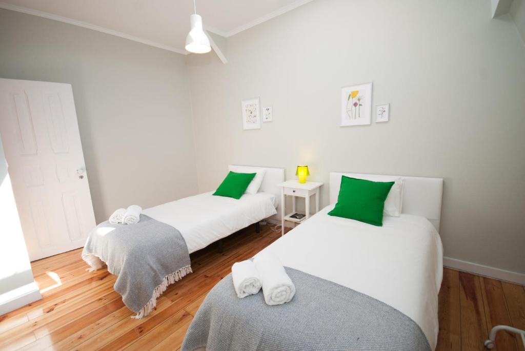 Two single beds with white linens, green pillows, gray throws, and a small white nightstand with a yellow lamp.