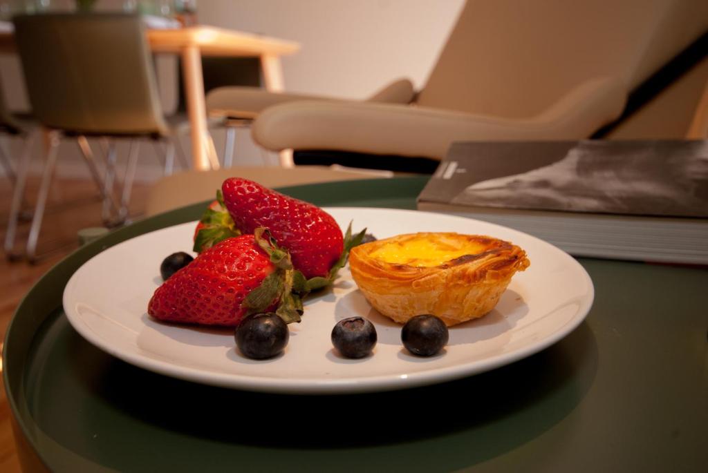 Plate with two strawberries, an egg tart, and five blueberries on a green table.