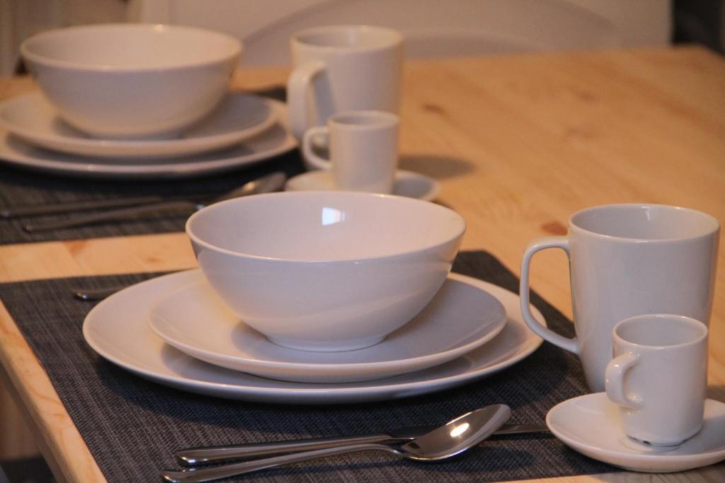 Two place settings with white bowls, plates, mugs, and spoons on a wooden table with dark placemats.