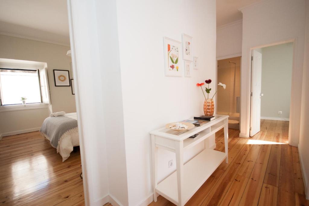 Hallway with wooden floor, white console table with vase and flowers, leading to bedroom and bathroom.