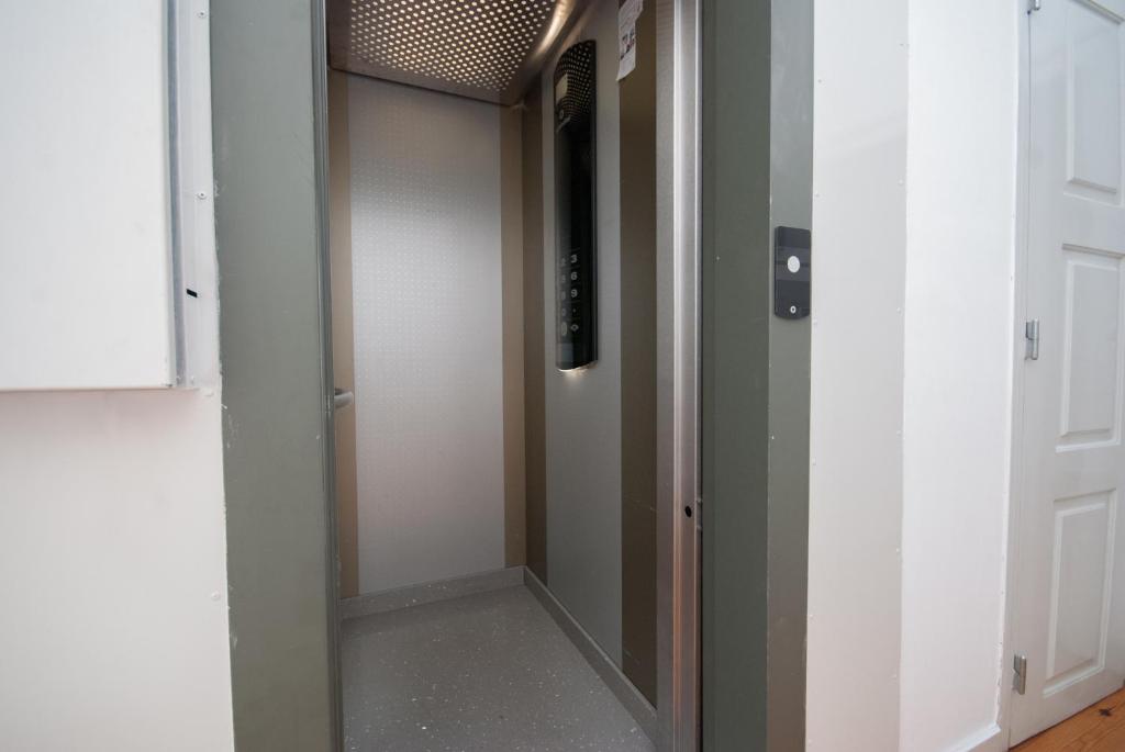 Open small residential elevator with closed panels, button panel inside, and white surrounding walls.