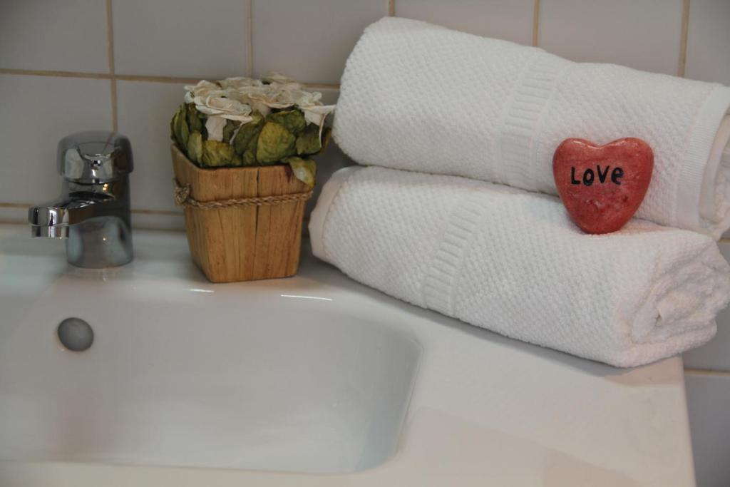 Two white rolled towels stacked on a sink with a red heart stone labeled 'Love' and a flower pot nearby.