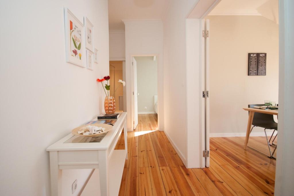 Bright hallway with wooden floors, white walls, console table with vase and flowers, and open door to dining room.