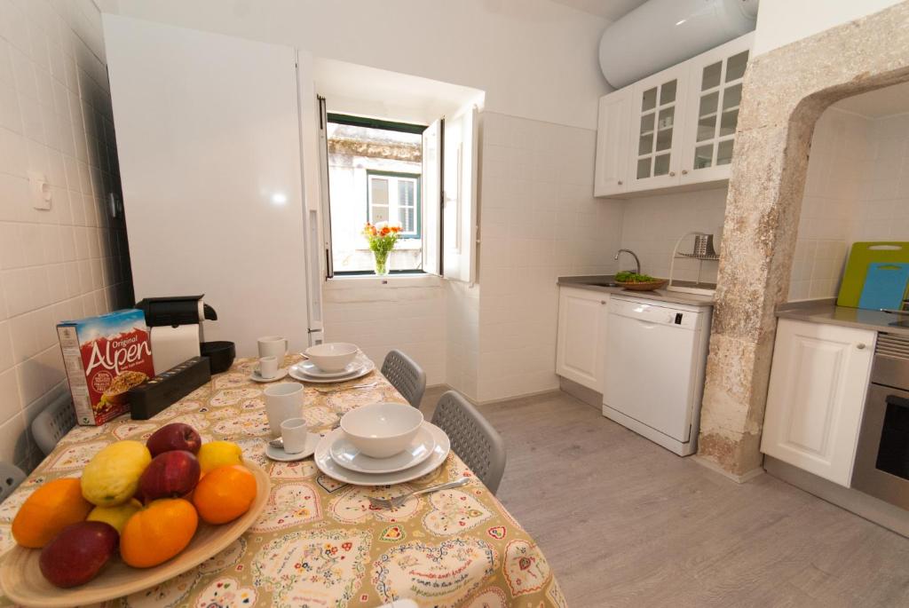 Bright kitchen with wooden floor, table set with bowls, fruit, cereal box, coffee maker, and window with flowers.
