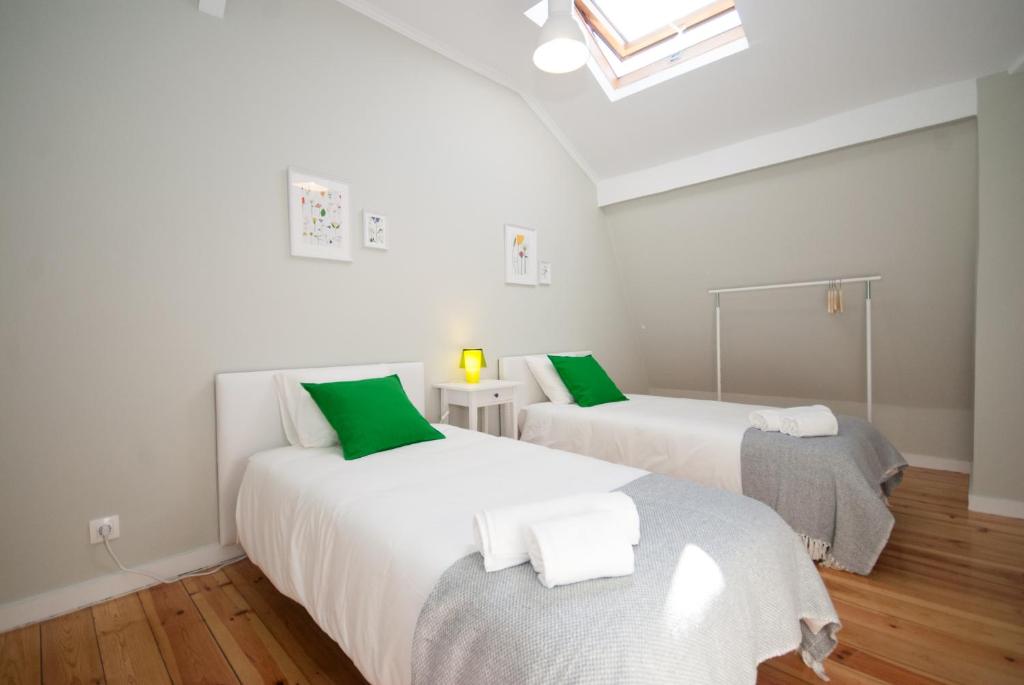 Minimalist bedroom with two single beds with green pillows, white linens, gray blankets, wooden floor.