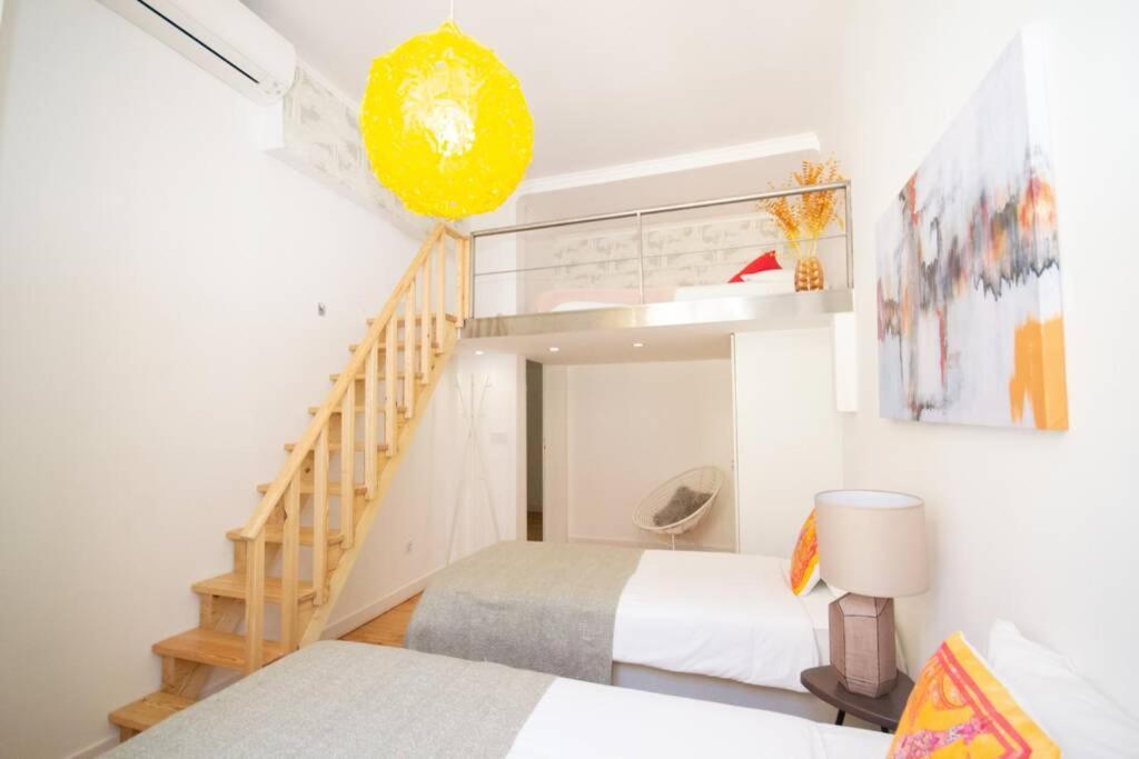 Bright room with two beds, wooden stairs to a loft, yellow pendant light, and colorful pillows.