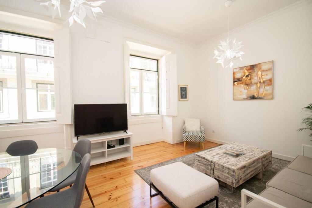 Bright living room with wooden floor, gray sofa, armchair, square coffee table, TV, and glass dining table.