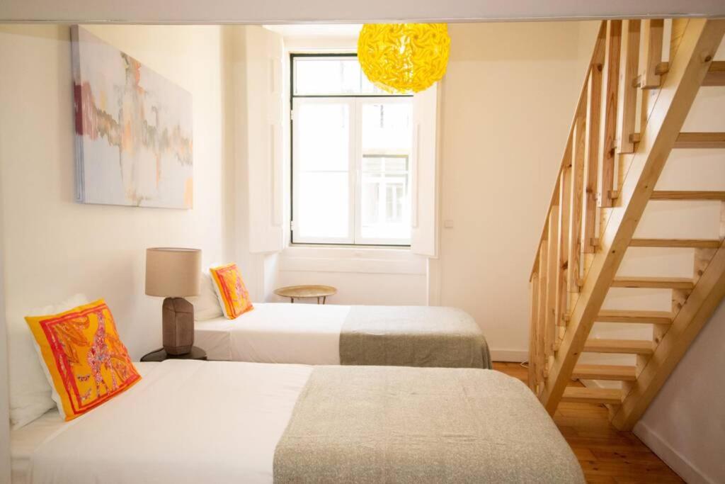 Bright bedroom with two single beds, colorful pillows, wooden stairs, and a yellow hanging lamp.