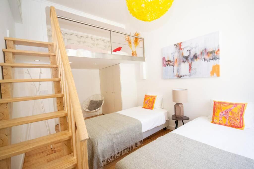 Bright bedroom with two single beds, colorful pillows, wooden loft stairs, and abstract wall art.