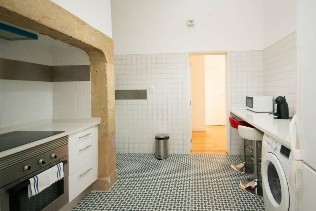 Bright kitchen with patterned floor, white cabinets, oven, washing machine, microwave, and two bar stools.