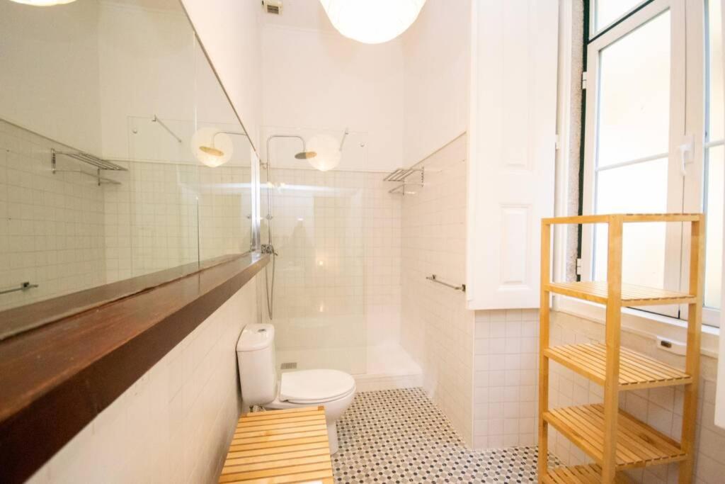 Bright bathroom with shower, toilet, large mirror, wooden shelving unit, and tiled floor.