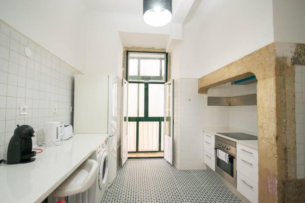 Bright white kitchen with black and white tiled floor, appliances, and an open door to a balcony.