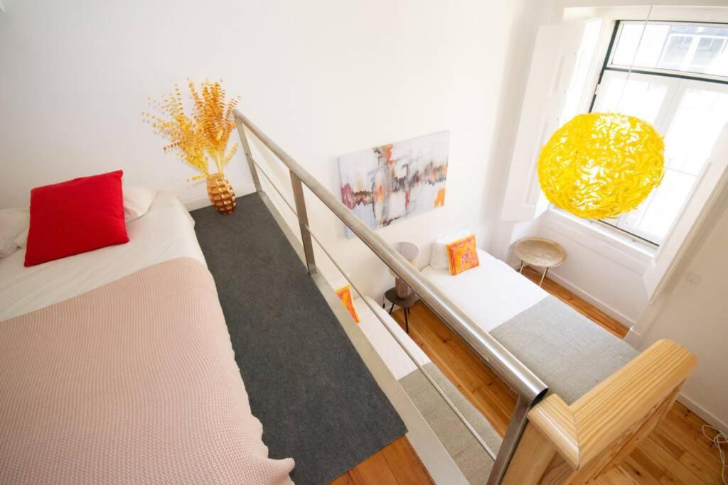 Bright loft bedroom with two beds, red and orange pillows, yellow lamp, and modern railing.