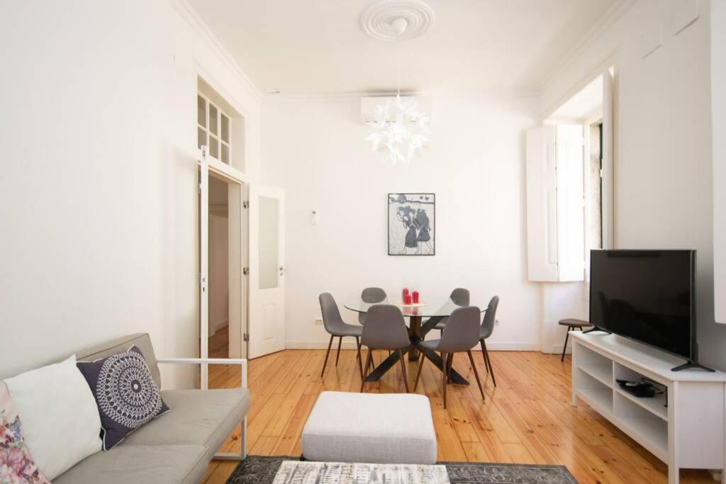 Bright living room with gray sofa, glass dining table with chairs, TV on white stand, and wooden floor.