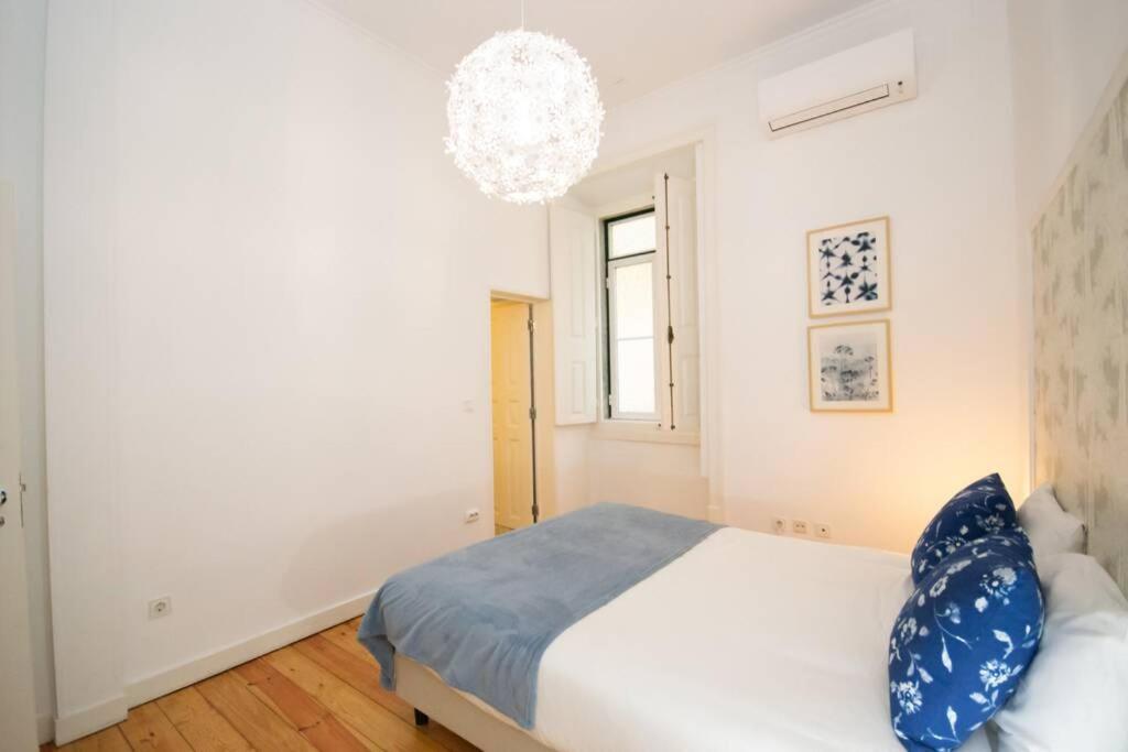Bright bedroom with white walls, wooden floor, blue pillows and blanket, round ceiling light, and air conditioner.