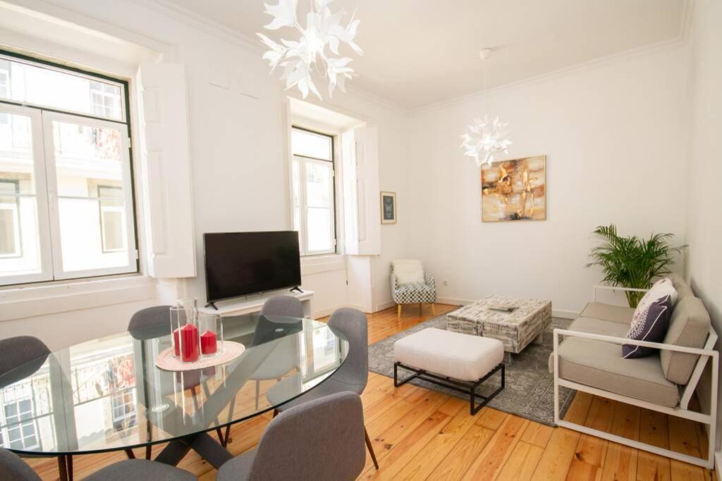 Bright living room with glass dining table, gray chairs, sofa, ottoman, TV, and potted plant.