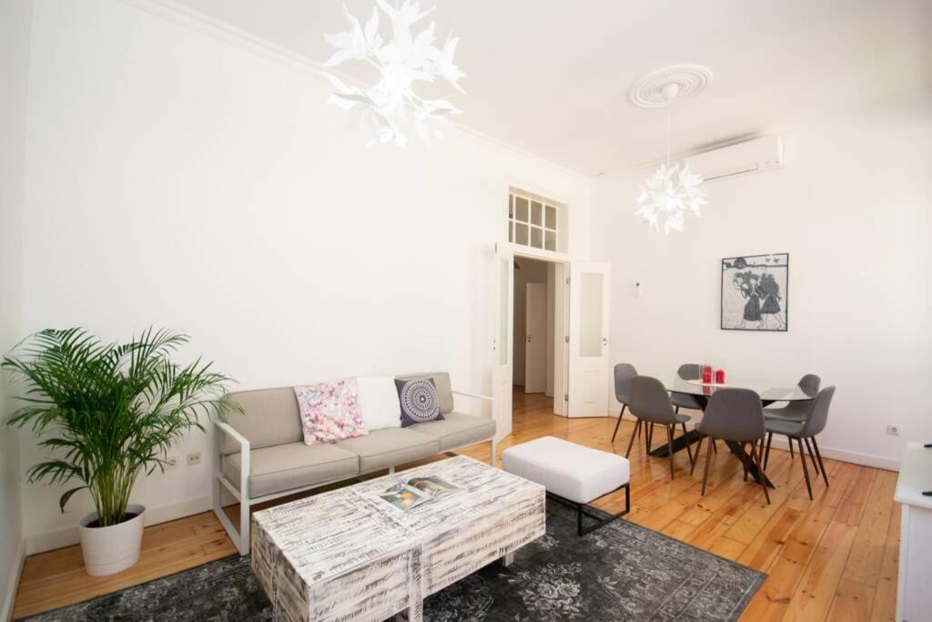 Bright living room with gray sofa, patterned pillows, white wooden coffee table, and round dining table with chairs.