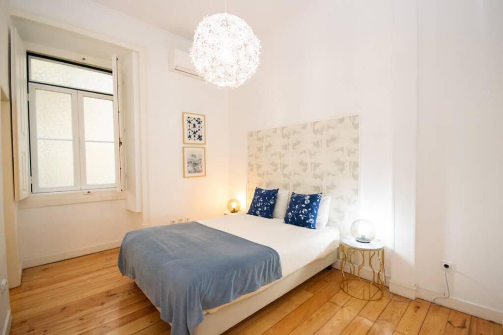 Minimal bedroom with wood floor, white walls, floral headboard, white bed, blue pillows, and round lamps.
