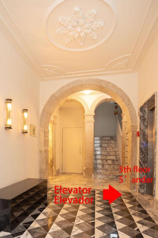 Marble floor and stairs under a stone arch with ceiling decor, benches, and elevator with red directional text.
