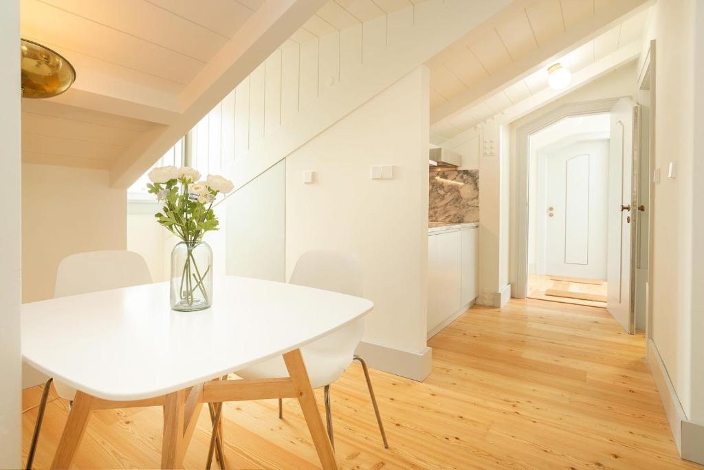 Bright kitchen corner with white table, chairs, vase with flowers, wooden floor, and open door.