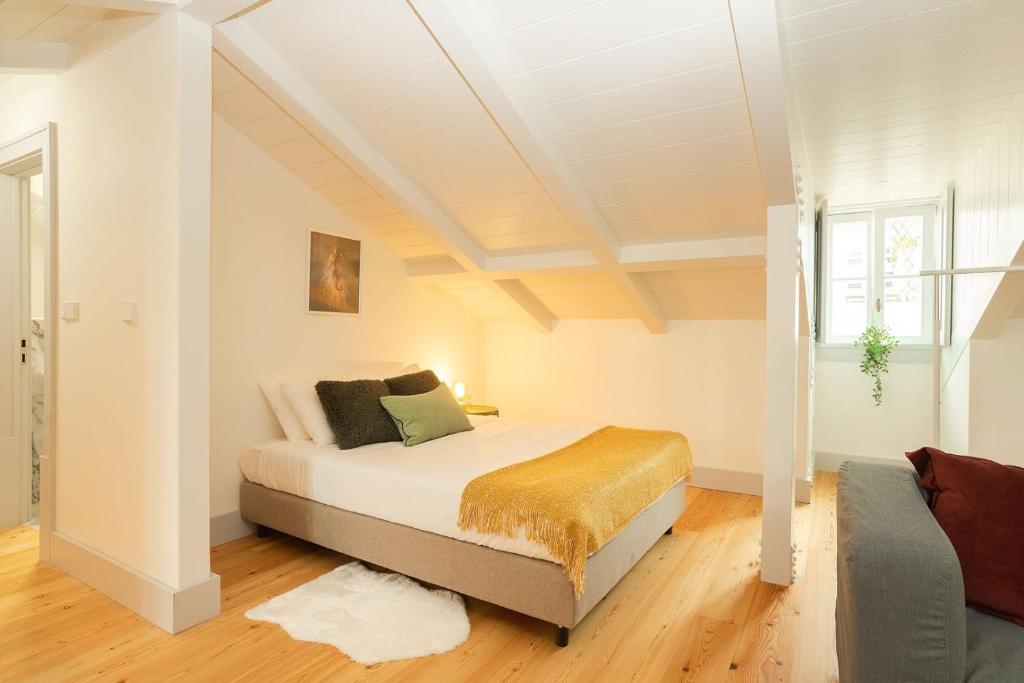 Cozy attic bedroom with slanted white ceiling, bed with pillows and yellow throw, wooden floor, and window plant.