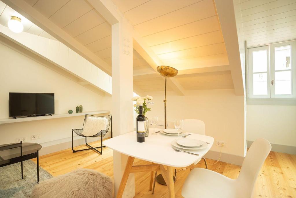 Bright dining area in attic with white table, chairs, wine bottle, plates, and TV in the background.
