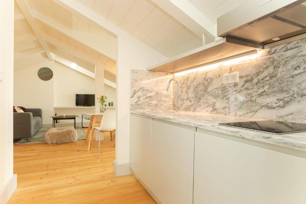 Modern kitchen with white cabinets, marble countertop, induction stove, and view into a living area with a gray sofa.