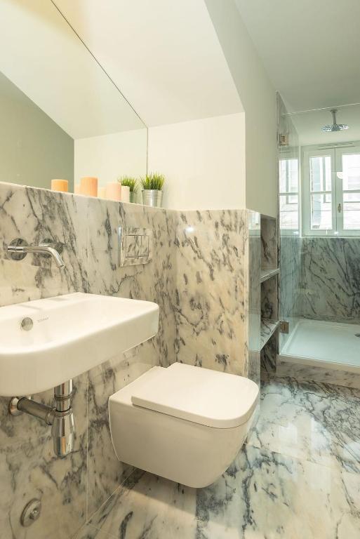 Modern bathroom with wall-mounted toilet, white sink, marble walls and floor, and glass shower enclosure.