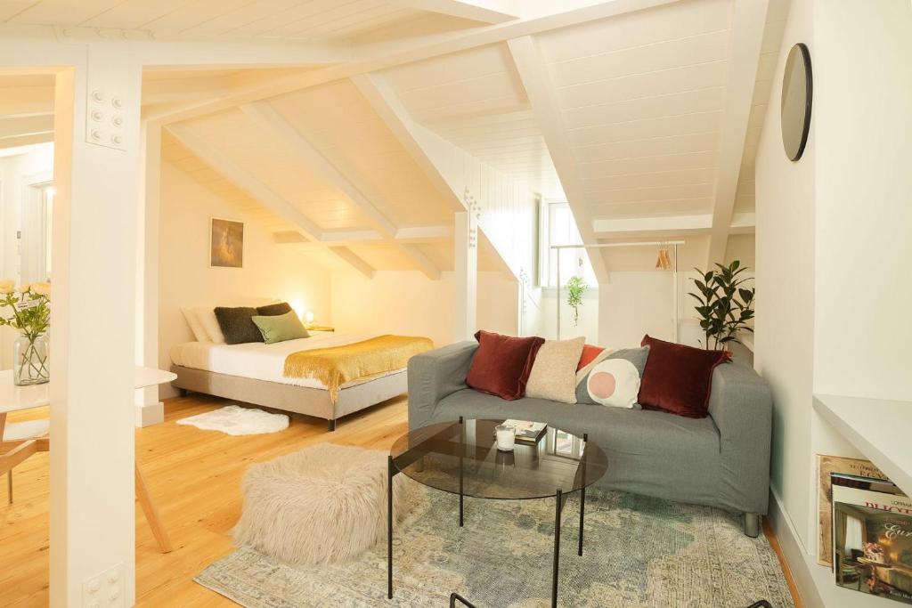 Cozy attic room with a bed, gray sofa, round glass coffee table, and light wooden flooring.