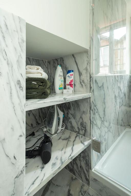 Marble bathroom shelves with towels, shampoo, conditioner, an iron, and a hairdryer next to a glass shower.