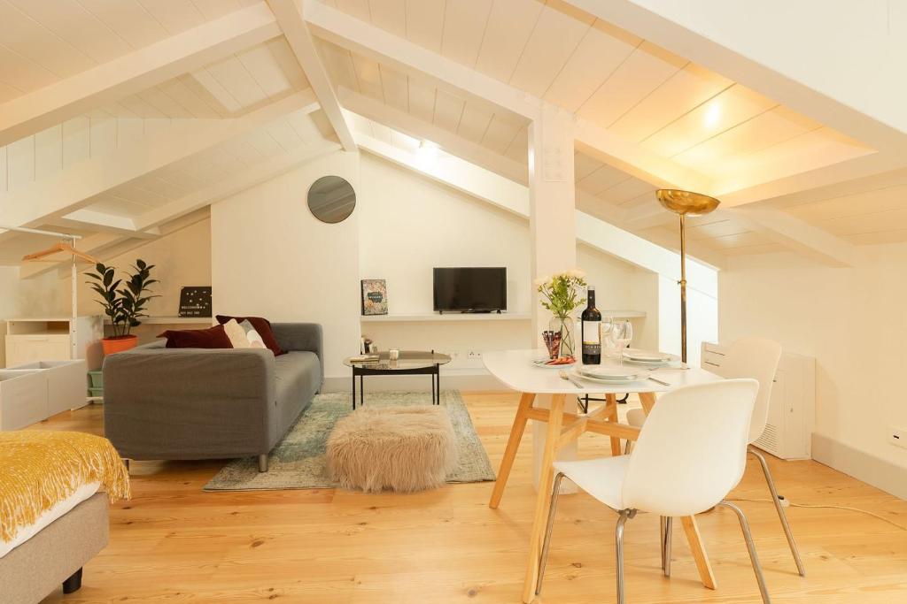 Bright attic living space with gray sofa, dining table set, plant, and wall-mounted TV under sloped ceiling.