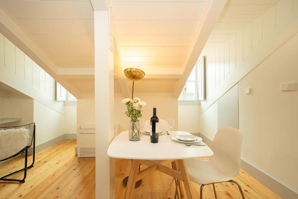 Cozy attic dining area with a white table, chair, wine bottle, flowers, and angled ceiling beams.