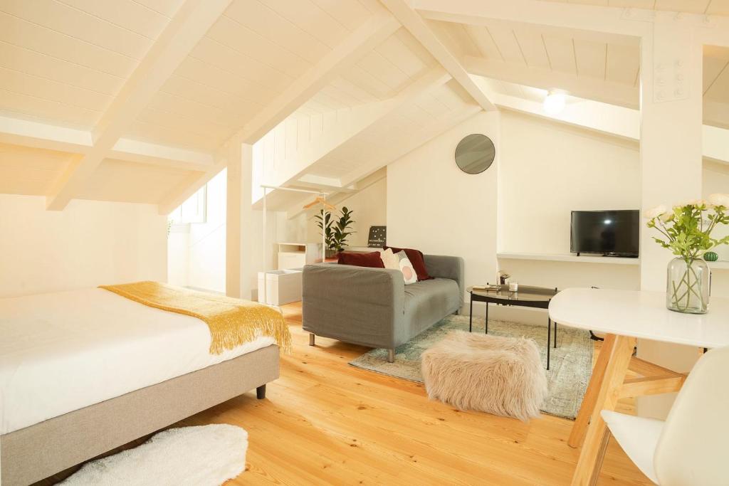 Bright attic room with a bed, gray sofa, furry ottoman, and white table with flowers.