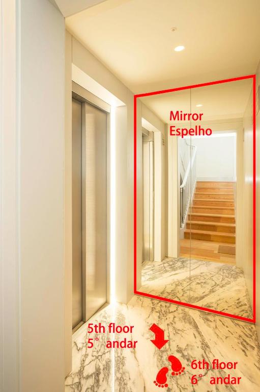 Hallway with elevator door and mirrored wall reflecting wooden stairs inside the building.