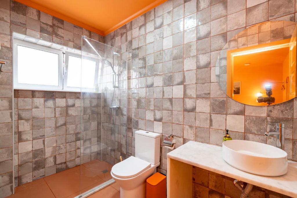 Bathroom with gray tiled walls, white toilet, round mirror, and white sink on marble countertop.