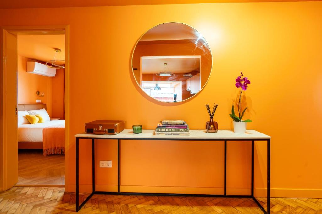 Orange wall with a round mirror above a table holding books, a plant, candle, and a small suitcase.