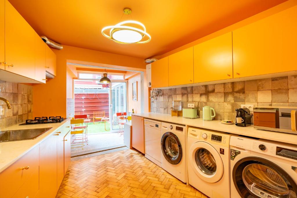Bright orange kitchen with white appliances, washing machines, and a view of outdoor seating area.
