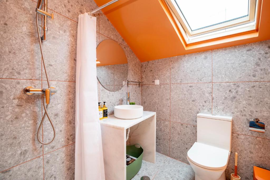 Compact bathroom with gray tiled walls, white toilet, round mirror, marble sink, and an orange skylight ceiling.